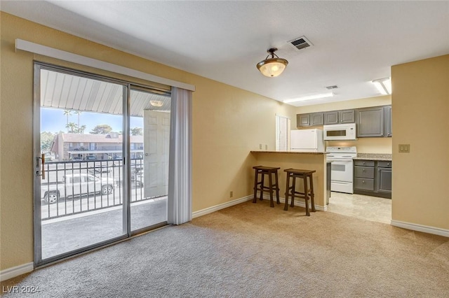 kitchen with a breakfast bar, light colored carpet, visible vents, gray cabinetry, and white appliances