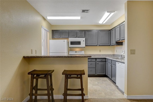 kitchen featuring white appliances, visible vents, a breakfast bar area, a peninsula, and gray cabinets