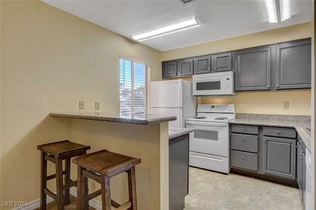 kitchen with light stone counters, a breakfast bar area, a peninsula, white appliances, and gray cabinets