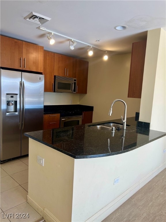 kitchen with sink, kitchen peninsula, dark stone countertops, light tile patterned floors, and appliances with stainless steel finishes