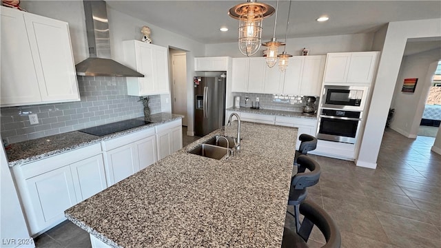 kitchen with a center island with sink, white cabinets, sink, wall chimney exhaust hood, and appliances with stainless steel finishes