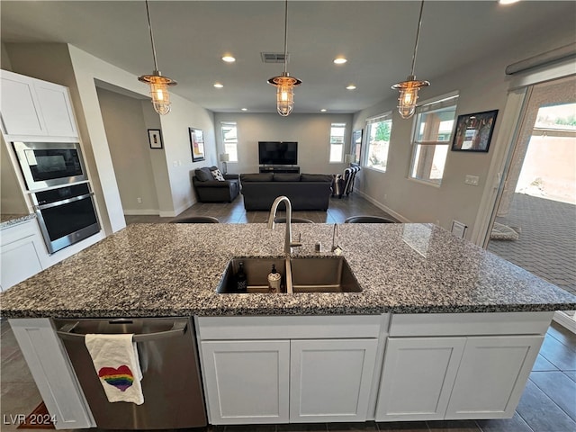 kitchen with sink, hanging light fixtures, an island with sink, white cabinetry, and stainless steel appliances