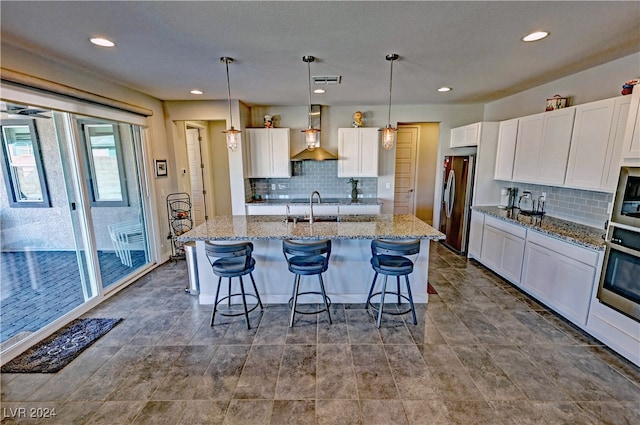 kitchen with appliances with stainless steel finishes, sink, decorative light fixtures, and wall chimney range hood