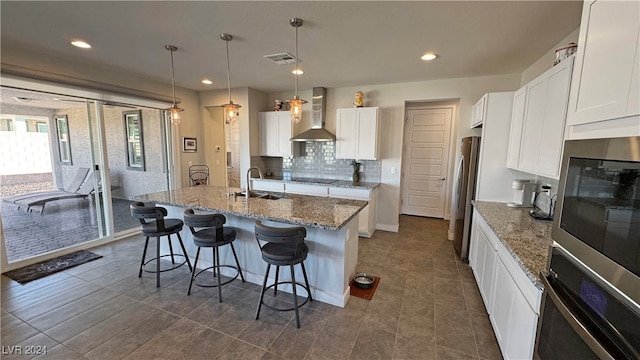 kitchen with wall chimney range hood, sink, appliances with stainless steel finishes, decorative light fixtures, and white cabinetry