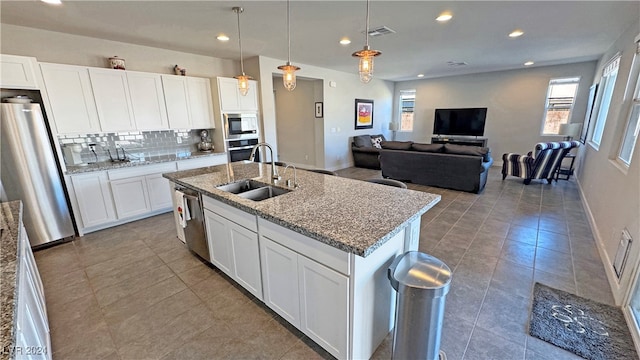 kitchen featuring stainless steel appliances, sink, decorative light fixtures, white cabinets, and an island with sink