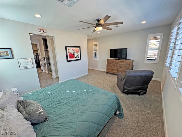 bedroom featuring a walk in closet, ceiling fan, and light colored carpet