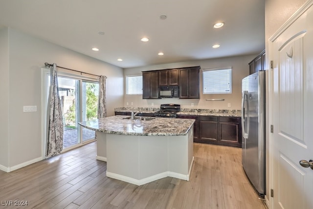 kitchen with light stone countertops, an island with sink, light hardwood / wood-style floors, and black appliances