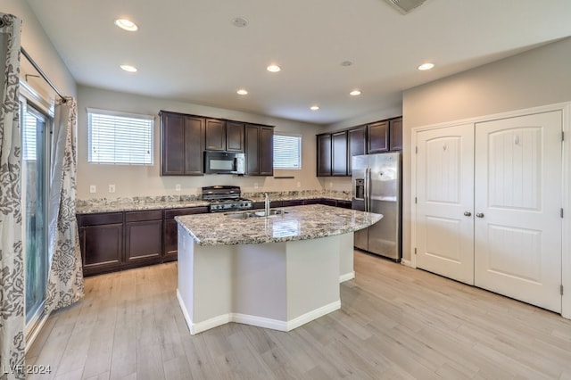 kitchen featuring light wood-type flooring, light stone counters, sink, black appliances, and a center island with sink