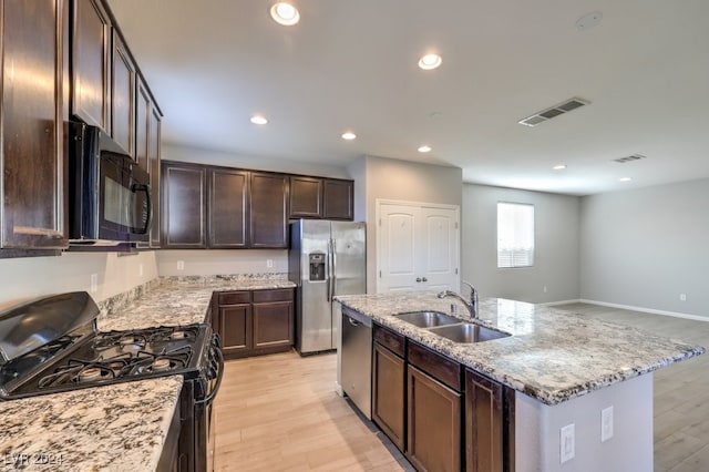 kitchen featuring light stone counters, a kitchen island with sink, sink, black appliances, and light hardwood / wood-style flooring