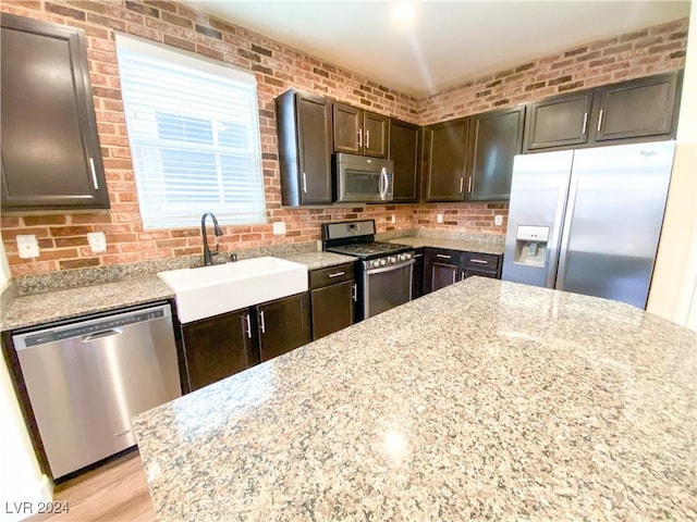 kitchen featuring dark brown cabinetry, light stone countertops, sink, light hardwood / wood-style floors, and appliances with stainless steel finishes