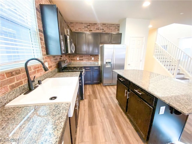 kitchen with light stone countertops, sink, a center island, appliances with stainless steel finishes, and light wood-type flooring