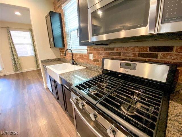 kitchen featuring light stone countertops, appliances with stainless steel finishes, light wood-type flooring, tasteful backsplash, and sink