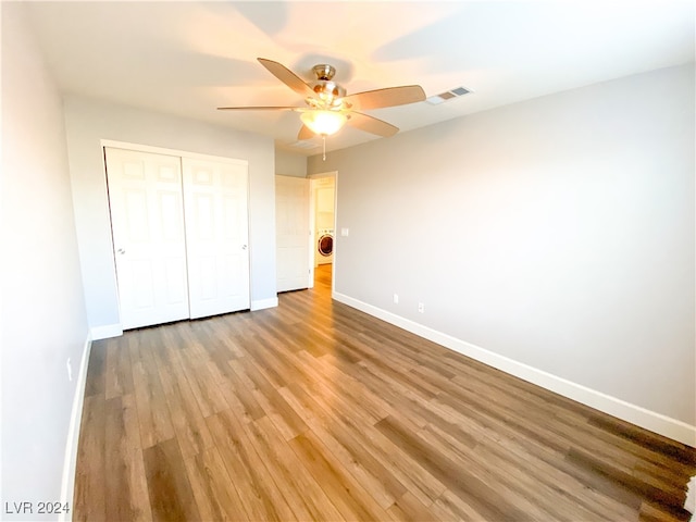 unfurnished bedroom with washer / clothes dryer, ceiling fan, a closet, and hardwood / wood-style flooring