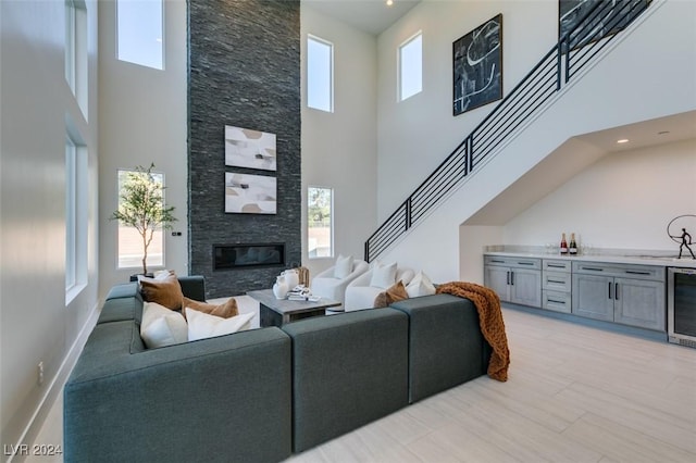 living room featuring a fireplace, a towering ceiling, a healthy amount of sunlight, and beverage cooler