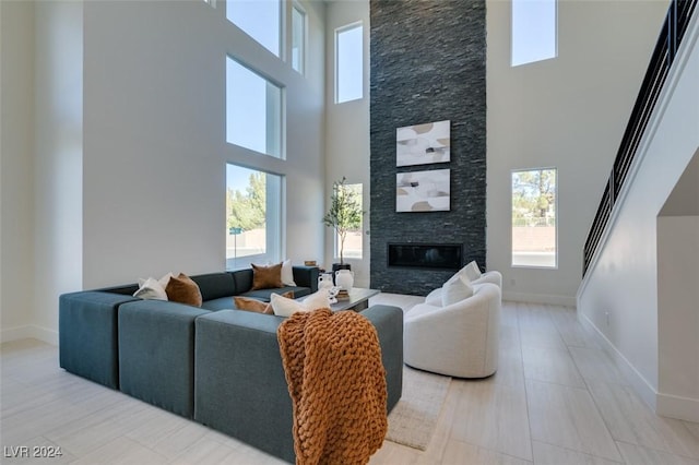 living room featuring a stone fireplace, a towering ceiling, and a wealth of natural light