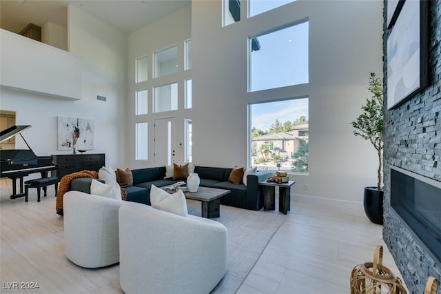 living room with light hardwood / wood-style floors, a stone fireplace, and a high ceiling