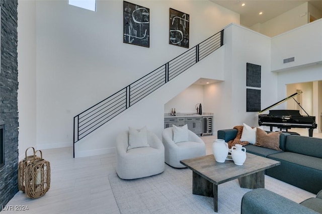 living room with a stone fireplace, a towering ceiling, sink, and beverage cooler