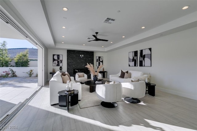 living room with a tray ceiling, ceiling fan, a fireplace, and light hardwood / wood-style flooring