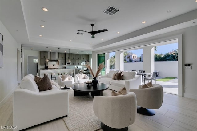 living room featuring a tray ceiling, ceiling fan, a healthy amount of sunlight, and light hardwood / wood-style floors