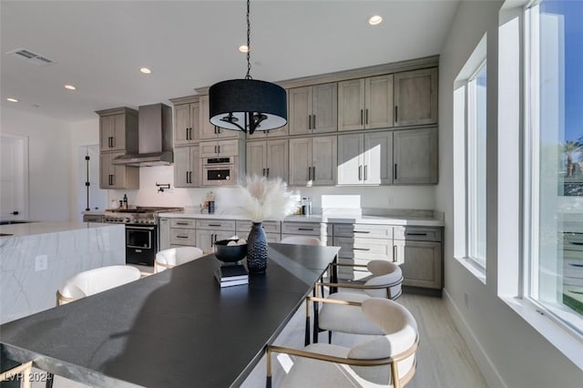 kitchen with hanging light fixtures, wall chimney exhaust hood, gray cabinets, light wood-type flooring, and appliances with stainless steel finishes