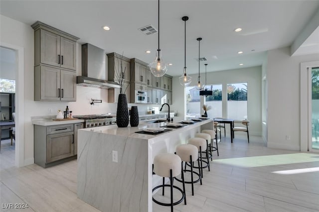 kitchen featuring appliances with stainless steel finishes, decorative light fixtures, a healthy amount of sunlight, and wall chimney range hood