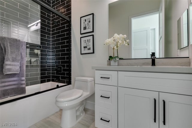 full bathroom with vanity, hardwood / wood-style flooring, toilet, and bath / shower combo with glass door