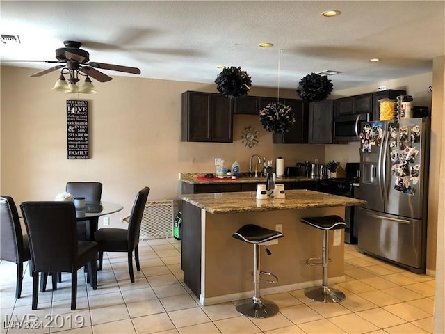 kitchen featuring stone counters, ceiling fan, appliances with stainless steel finishes, a kitchen island, and a kitchen bar