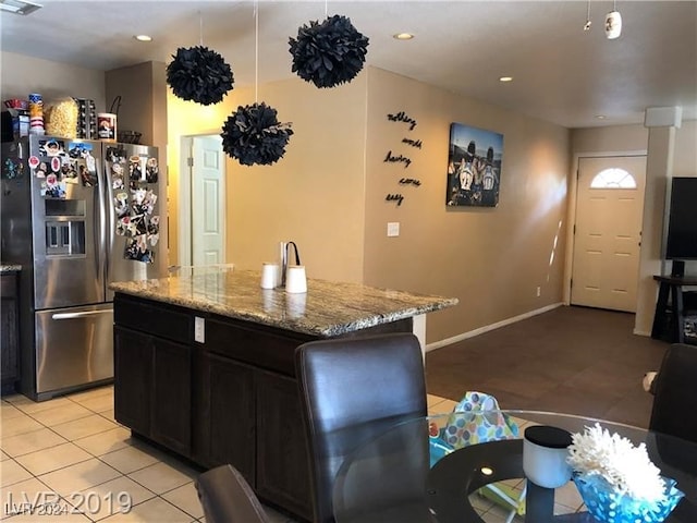 kitchen featuring stainless steel fridge with ice dispenser, light tile patterned floors, a kitchen island, and light stone counters