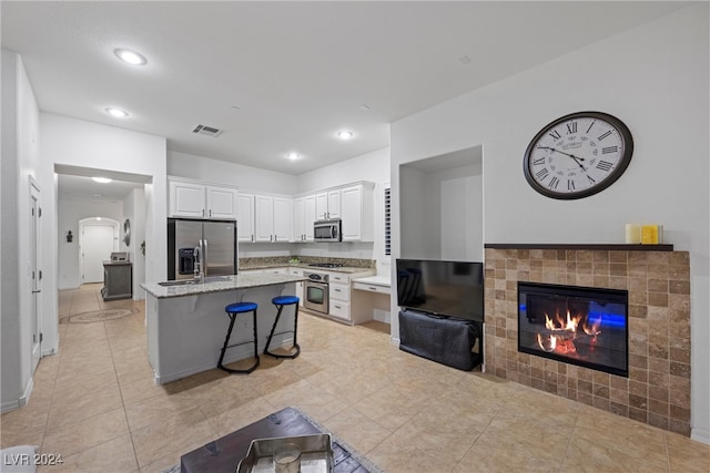 kitchen with a breakfast bar, stainless steel appliances, a kitchen island, white cabinetry, and a tiled fireplace