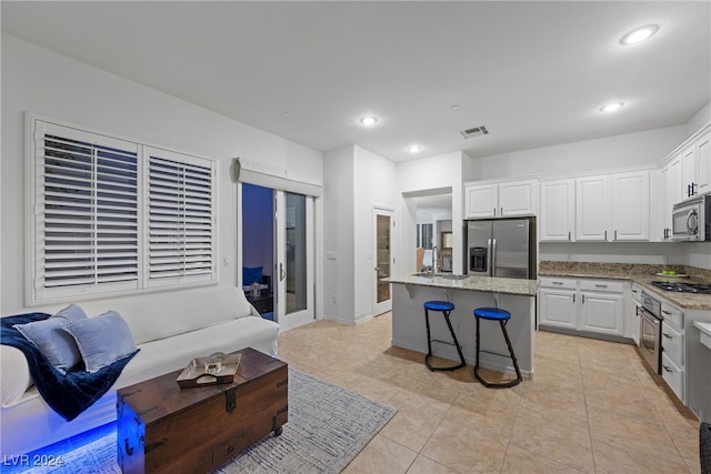 kitchen featuring light stone countertops, a center island, a kitchen bar, white cabinets, and appliances with stainless steel finishes