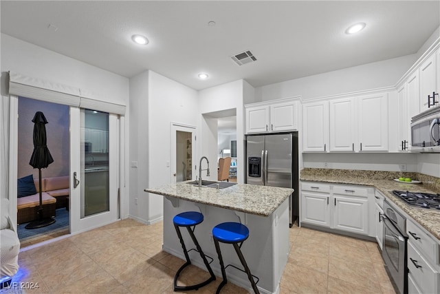 kitchen with light stone countertops, stainless steel appliances, sink, a center island with sink, and white cabinets