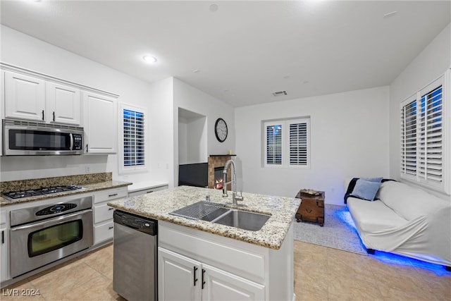 kitchen featuring stainless steel appliances, sink, light tile patterned floors, white cabinetry, and an island with sink