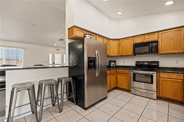 kitchen featuring a kitchen bar, kitchen peninsula, stainless steel appliances, lofted ceiling, and light tile patterned flooring