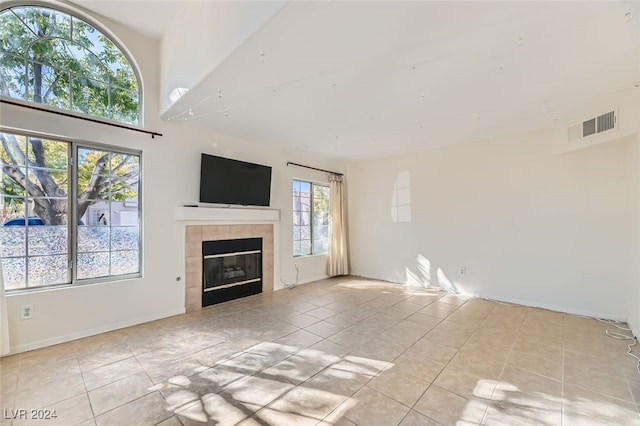 unfurnished living room with a tiled fireplace, a wealth of natural light, and light tile patterned floors