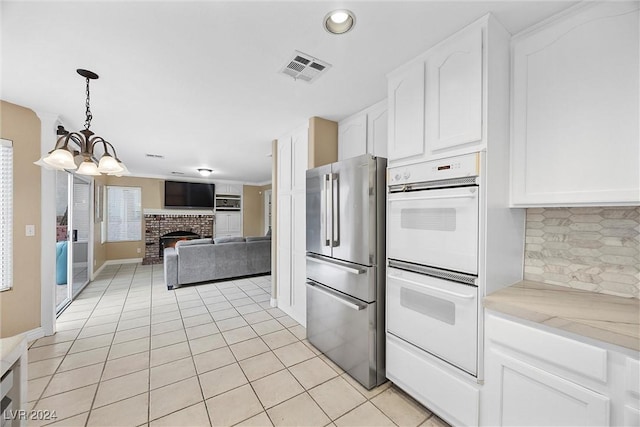 kitchen featuring white cabinets, a fireplace, double oven, a notable chandelier, and stainless steel refrigerator