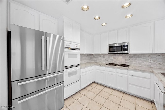 kitchen featuring tasteful backsplash, light stone counters, stainless steel appliances, light tile patterned floors, and white cabinets