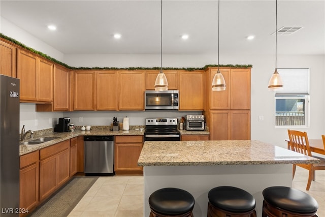 kitchen featuring sink, hanging light fixtures, light stone counters, a breakfast bar, and appliances with stainless steel finishes