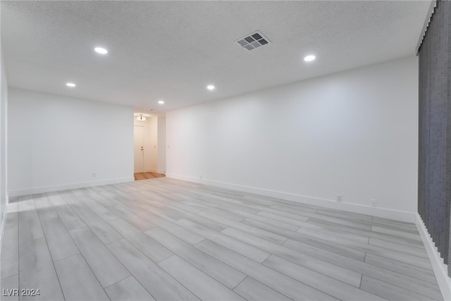 empty room with light wood-type flooring and a textured ceiling