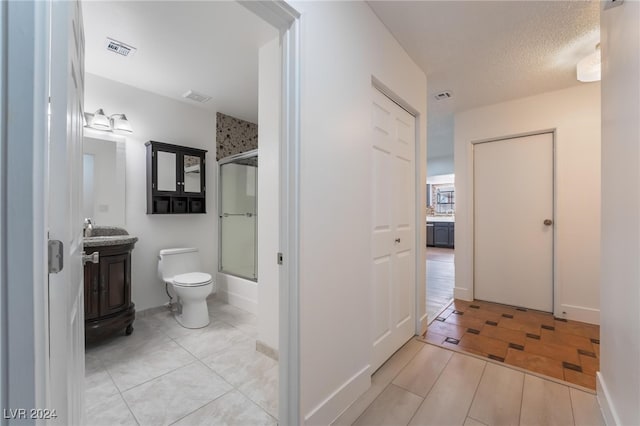 bathroom featuring tile patterned floors, a textured ceiling, toilet, and bath / shower combo with glass door