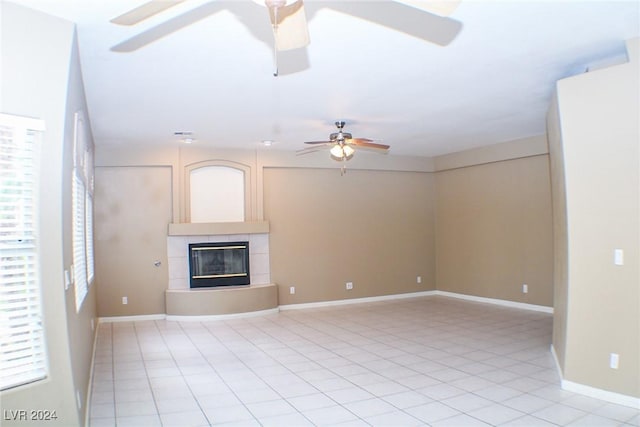 unfurnished living room with a tiled fireplace, light tile patterned floors, and ceiling fan