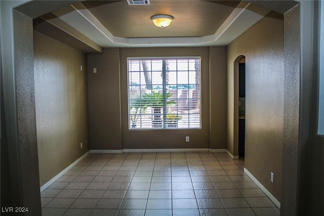 unfurnished room with tile patterned flooring and a raised ceiling