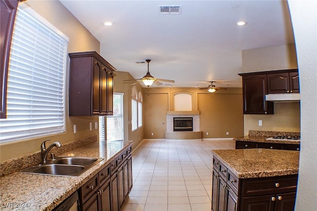 kitchen featuring sink, light tile patterned floors, gas cooktop, dark brown cabinetry, and a large fireplace