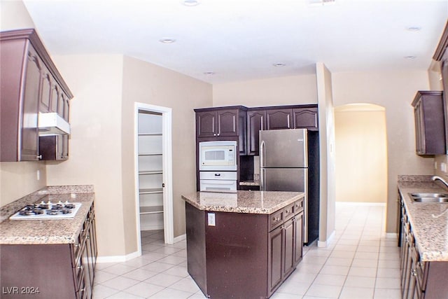 kitchen with dark brown cabinetry, sink, light tile patterned floors, and white appliances