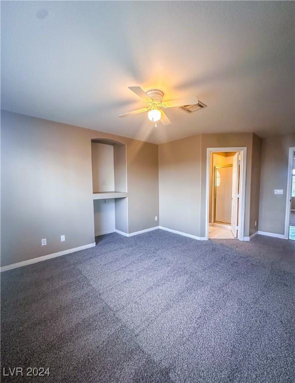 empty room with carpet flooring, ceiling fan, and built in shelves