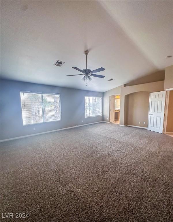 empty room with a wealth of natural light, vaulted ceiling, ceiling fan, and carpet