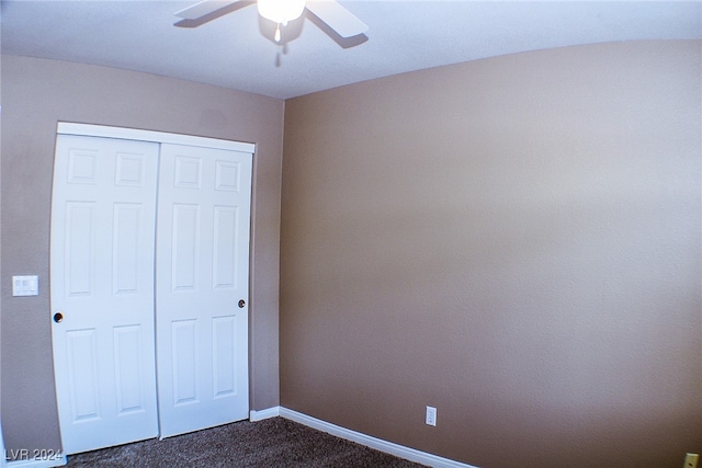 unfurnished bedroom with ceiling fan, dark carpet, and a closet