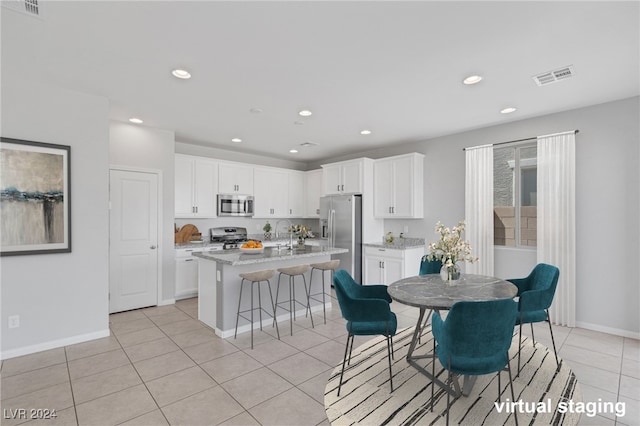 kitchen featuring white cabinets, light tile patterned floors, stainless steel appliances, and a kitchen island with sink