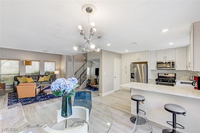 kitchen featuring hanging light fixtures, an inviting chandelier, light stone counters, white cabinets, and appliances with stainless steel finishes