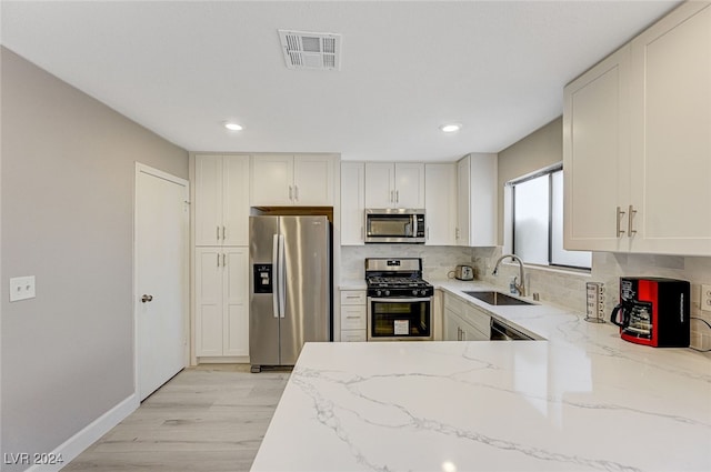 kitchen featuring sink, decorative backsplash, light wood-type flooring, light stone countertops, and appliances with stainless steel finishes