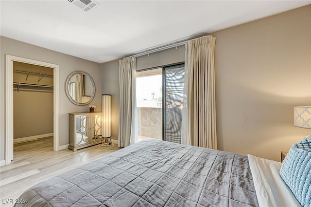 bedroom with light wood-type flooring, a walk in closet, access to outside, and a closet